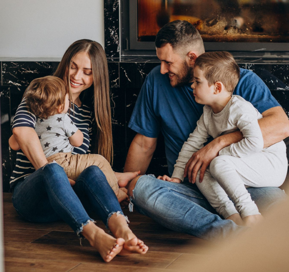Family sitting together on a living room floor, smiling and cuddling in a warm, cozy setting