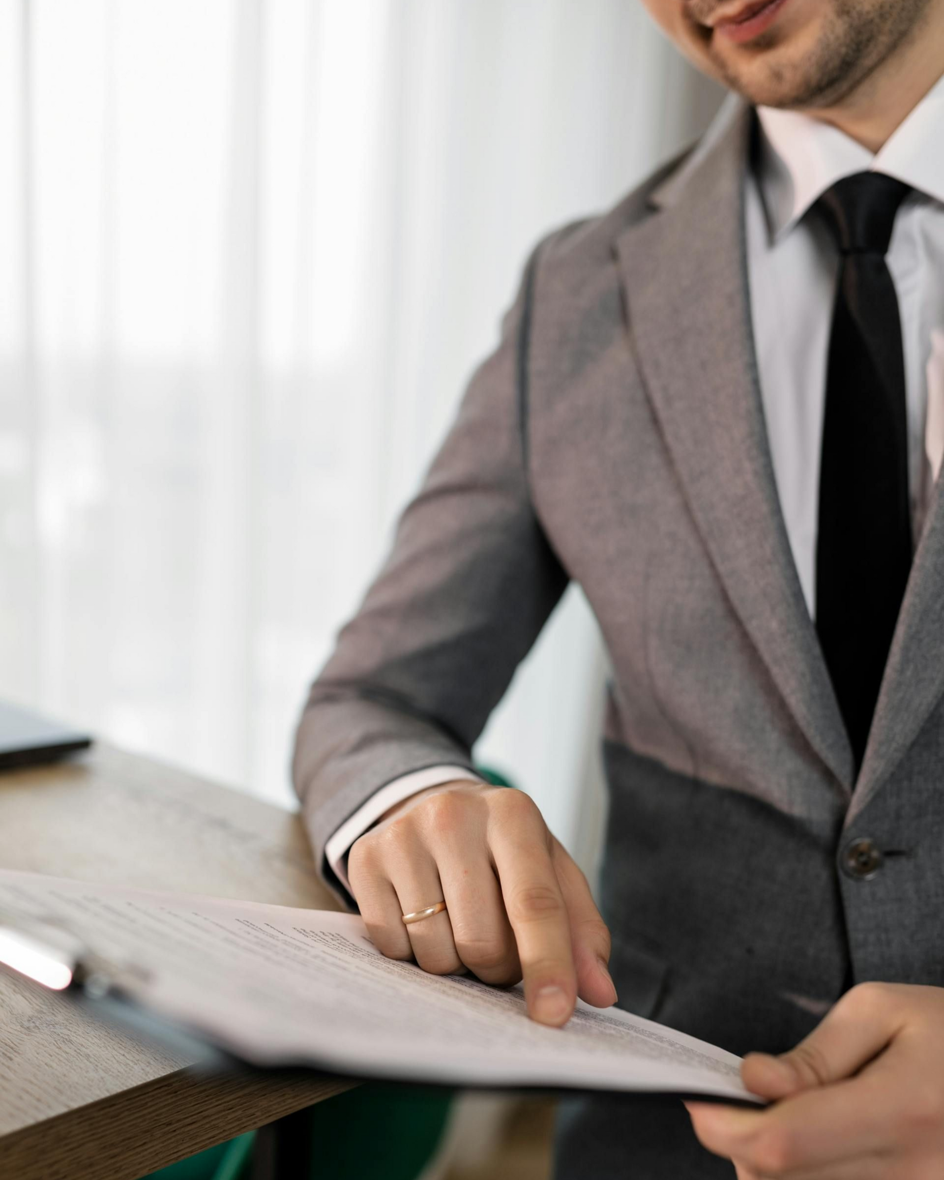 Person in a gray suit pointing at a document on a desk.
