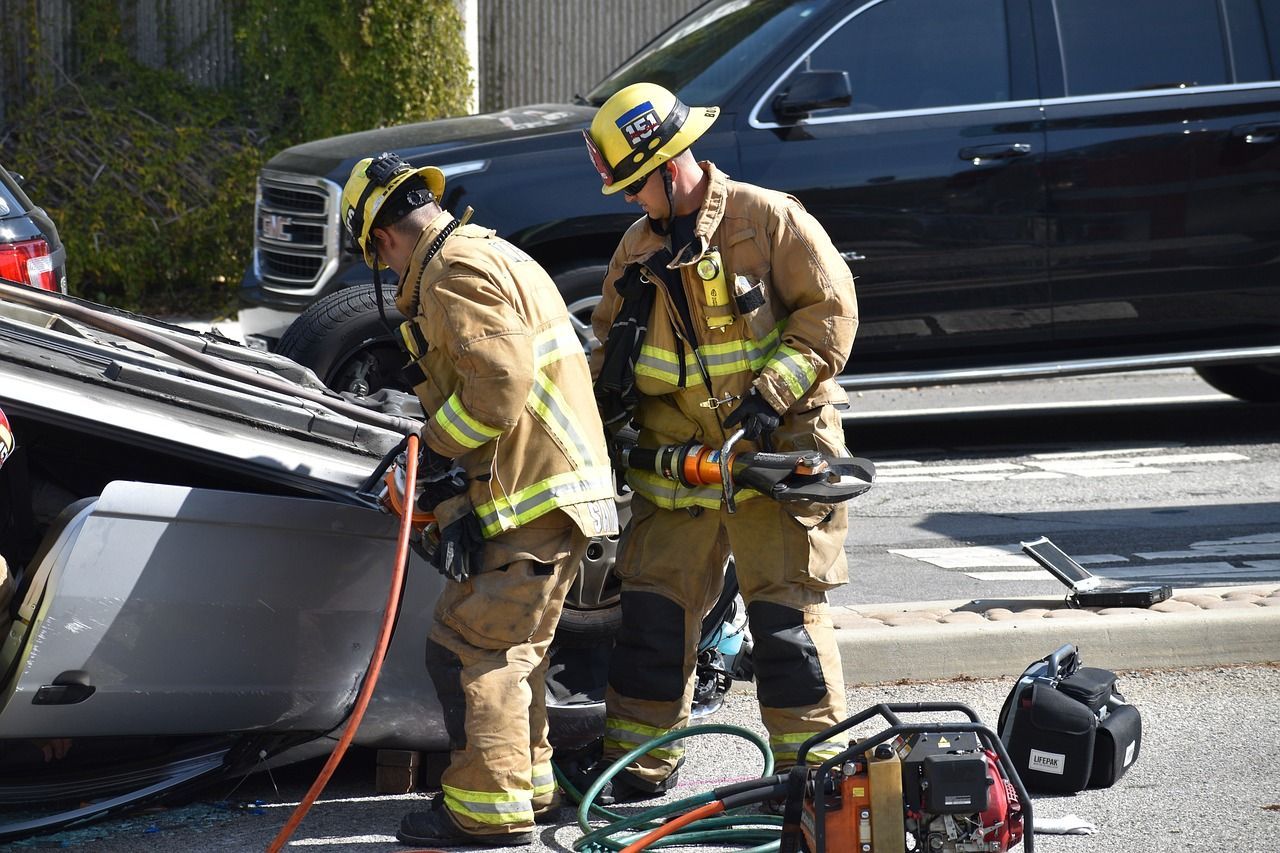Firefighters using rescue tools on a wrecked car. Scene on a street, a black SUV is in the background.