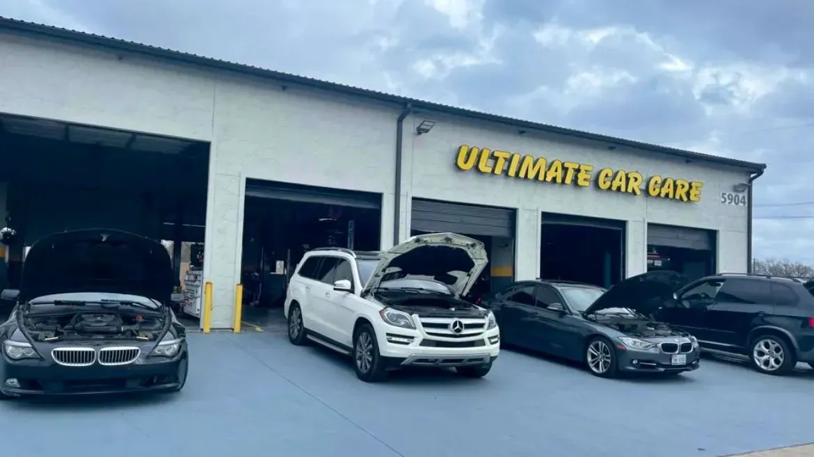 Four vehicles parked in front of an automotive shop named Ultimate Car Care, with several hoods open for maintenance.
