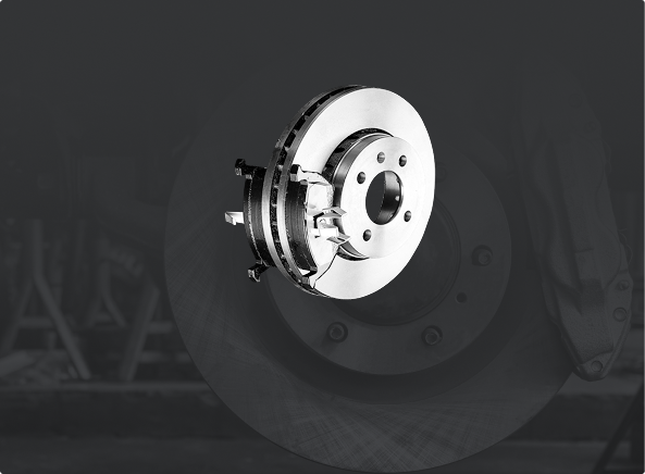 A metallic disc brake assembly with a caliper shown against a dark, out-of-focus background.