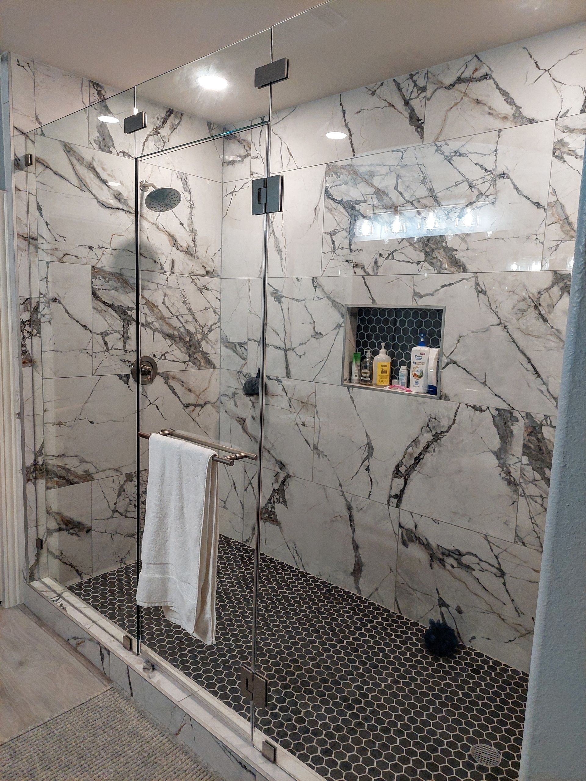 a bathroom with marble walls and a walk in shower with a glass door .