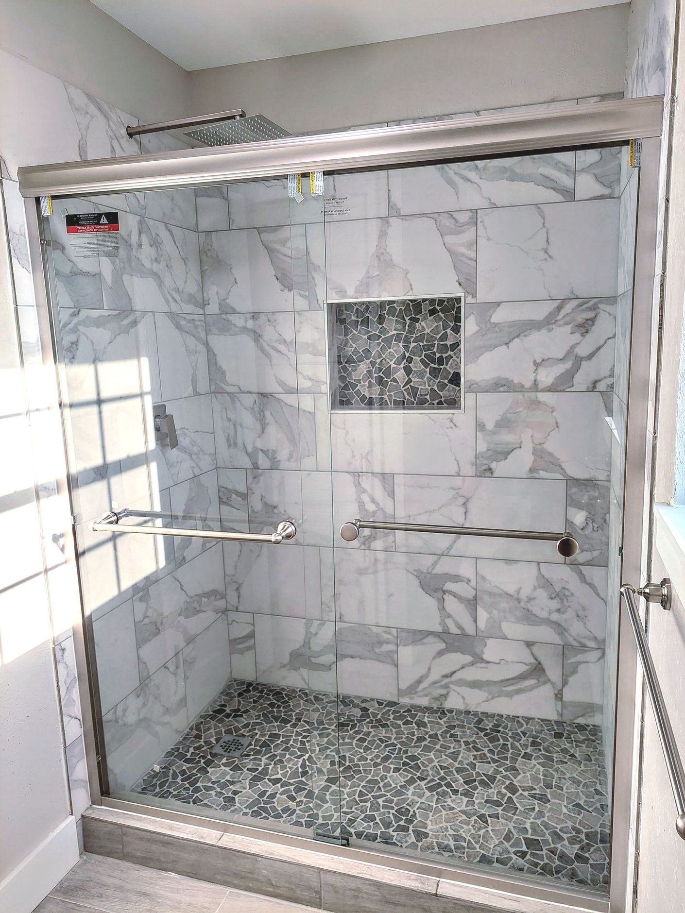 a bathroom with a walk in shower with marble tiles and a sliding glass door .