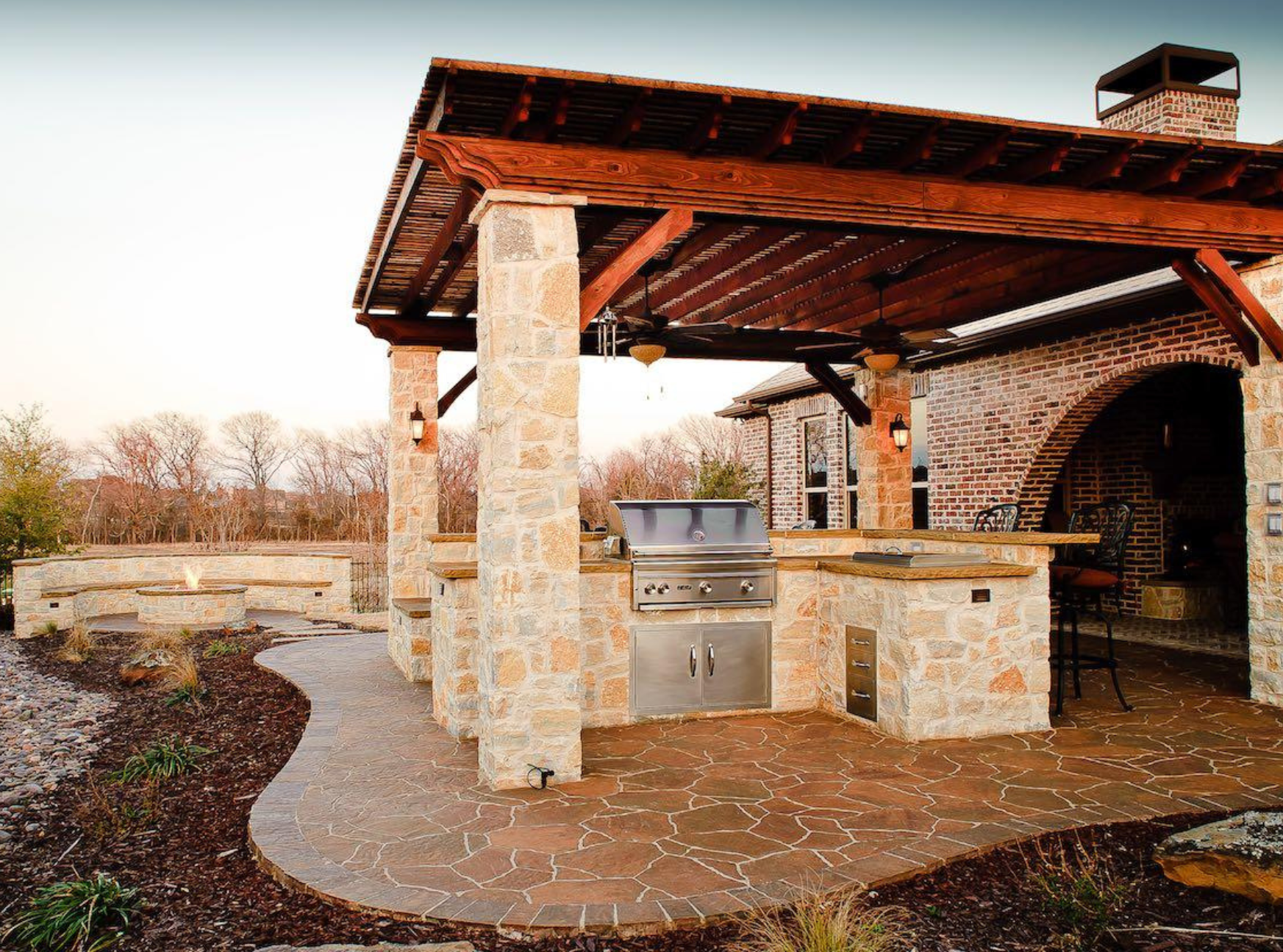 an outdoor kitchen with a wooden roof and stone pillars