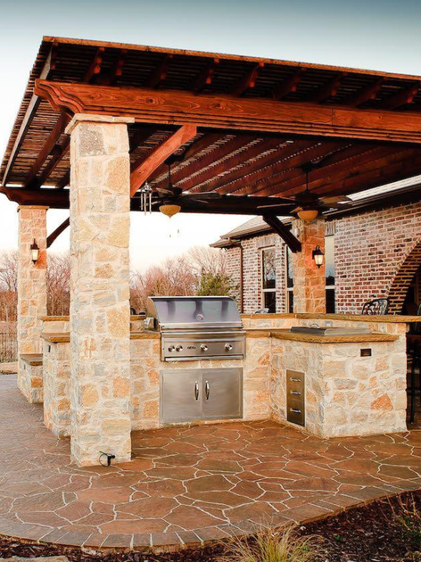 an outdoor kitchen with a wooden roof and stone pillars