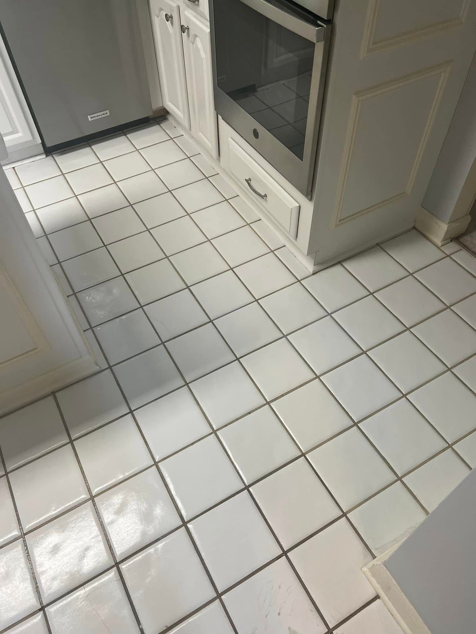 White tile kitchen floor with dark grout, beside a white cabinet and stainless steel appliance.