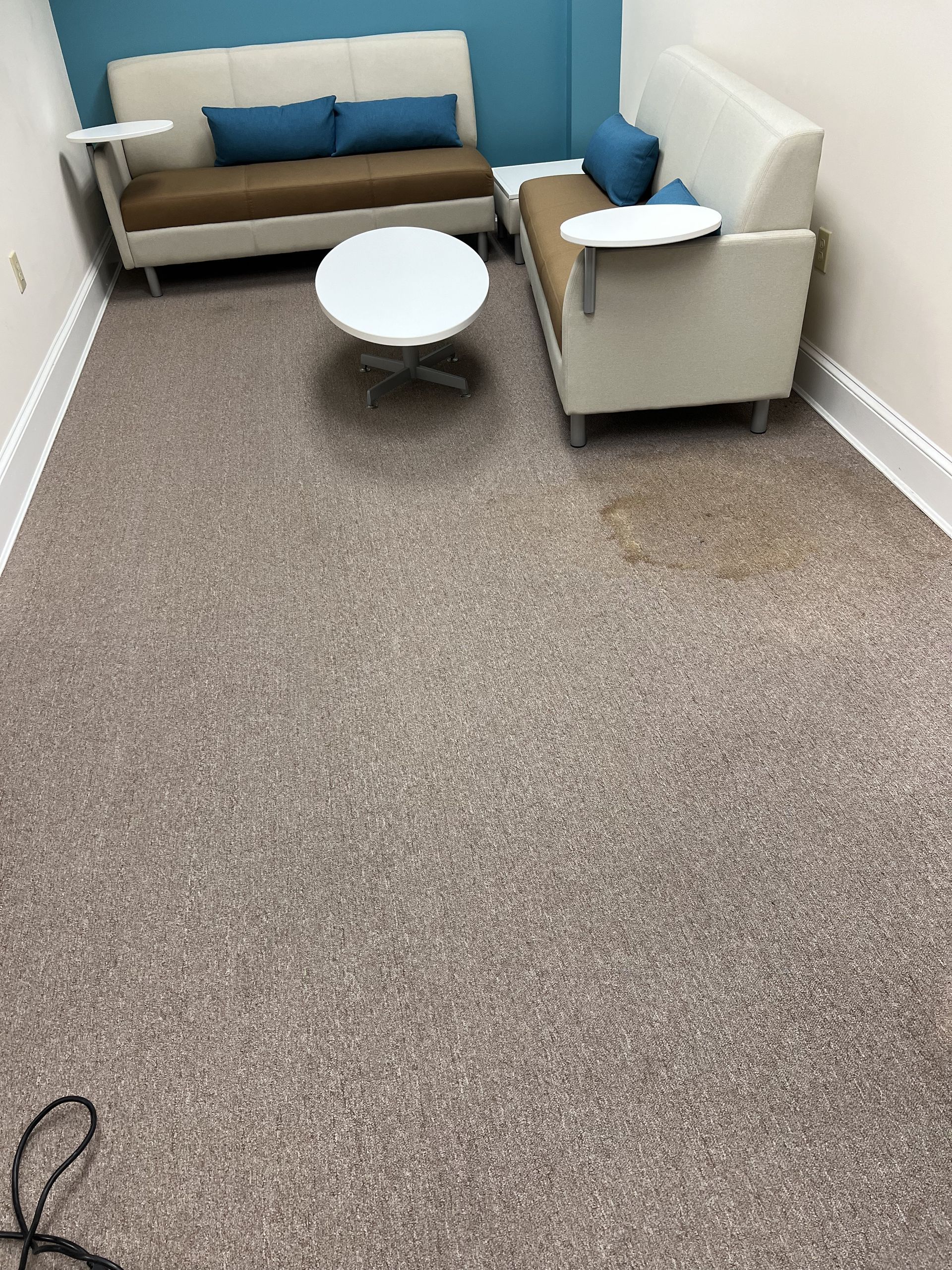 Waiting area with couches, round table, and stained carpet.
