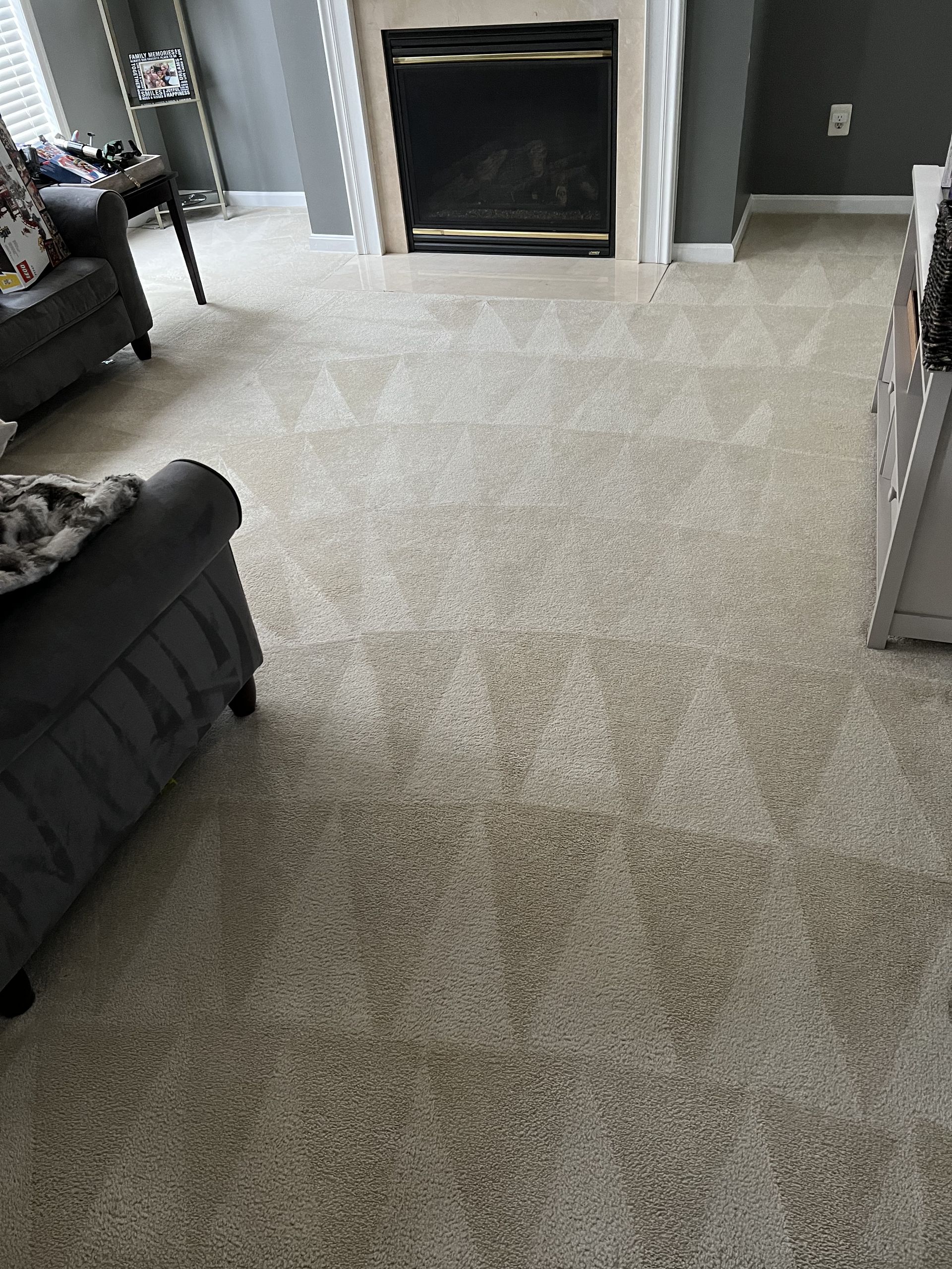 Beige carpet in a living room, fireplace at the back, gray furniture on the sides.