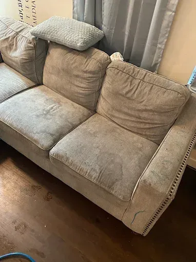 Beige fabric sofa with two cushions and a decorative border in a room with wood flooring.