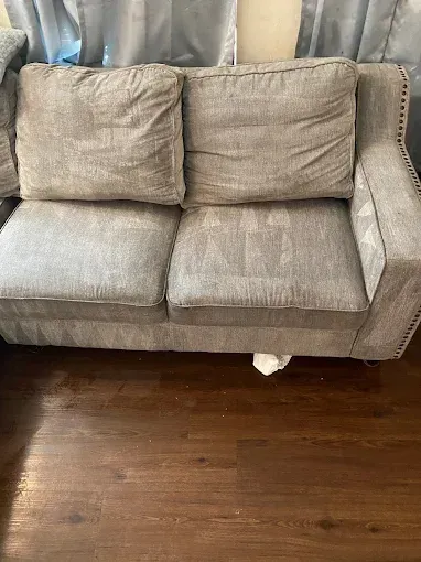 Gray upholstered loveseat with two cushions on dark wood floor, in front of a window.