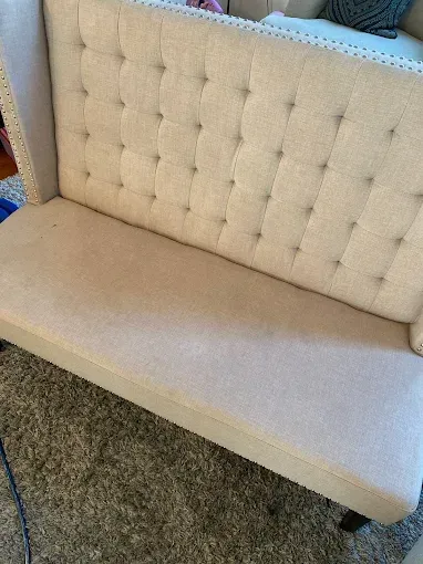 Beige tufted bench with high back, in a room with a rug.