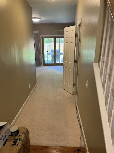 Hallway with beige carpet, tan walls, and a door open to a room with sliding glass doors.