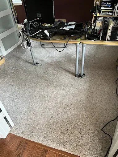 A cluttered desk with a computer and cables on light gray carpet in a room.