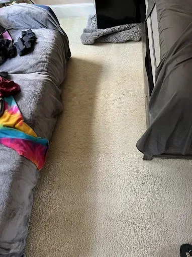 Bedroom with beige carpet between two beds, one with clothes on top.