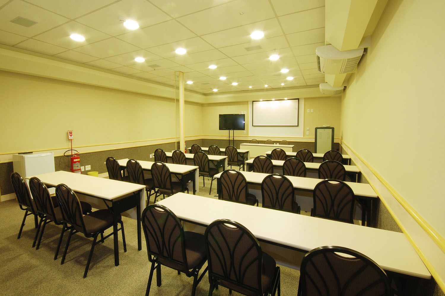 Uma sala de aula com mesas e cadeiras e uma tela de projetor