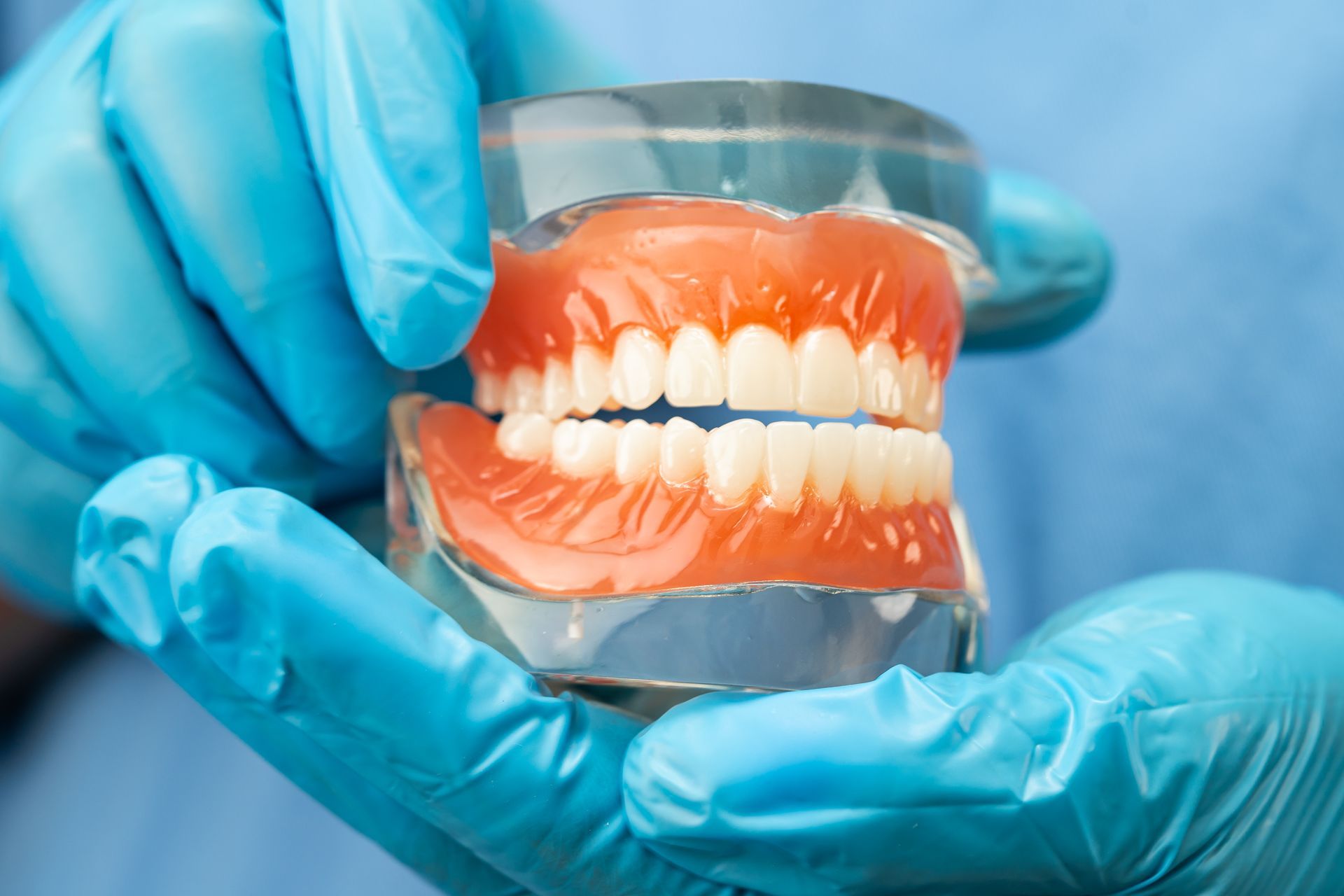 A dentist holding a removable denture model with upper and lower replacement teeth