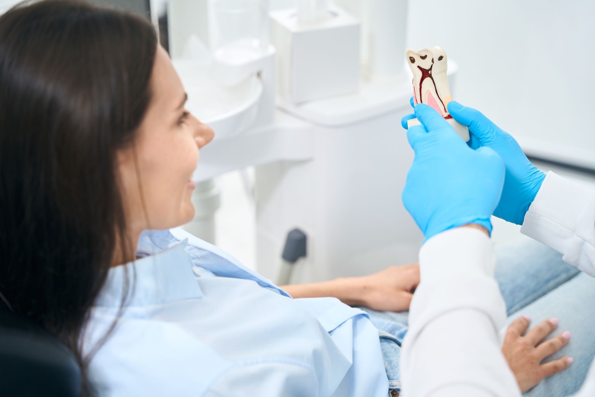 Dentist holding a tooth model while explaining treatment options to a patient during a consultation.