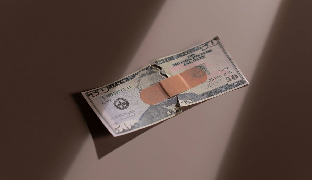 Two torn U.S. dollar bills taped together, lying on a brown surface with light shadows.