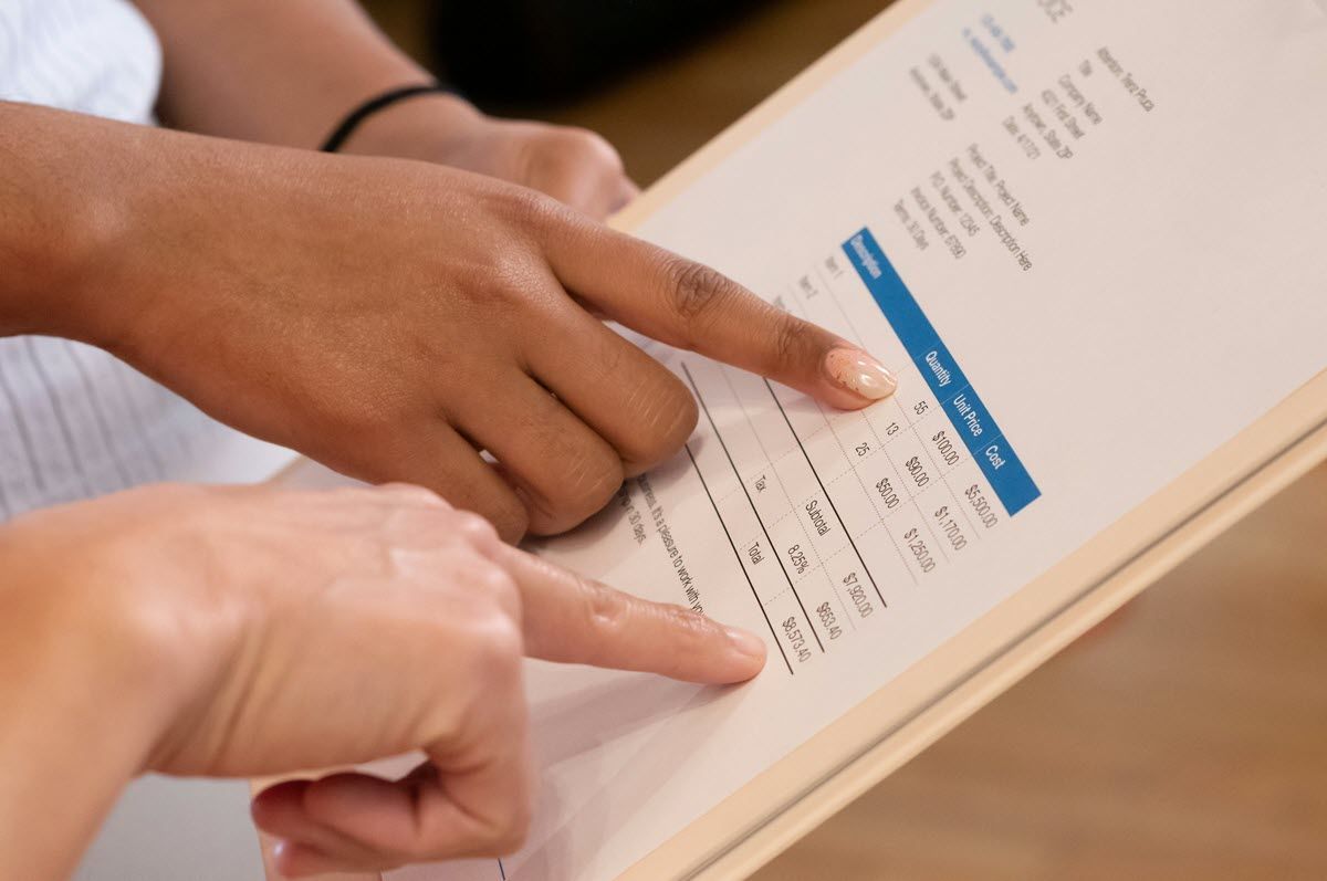 Two hands pointing at a document with a blue heading and table on a desk
