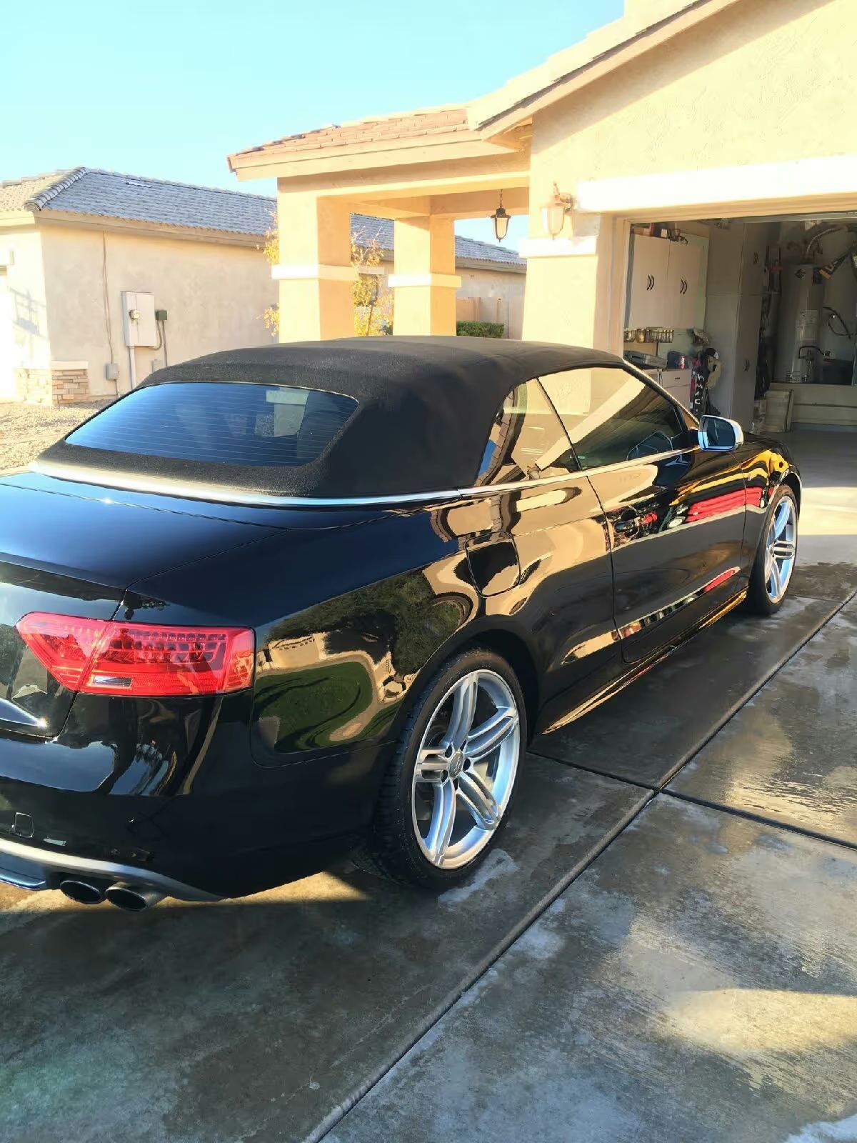 Black convertible parked in a driveway beside a house, seen from the rear side.