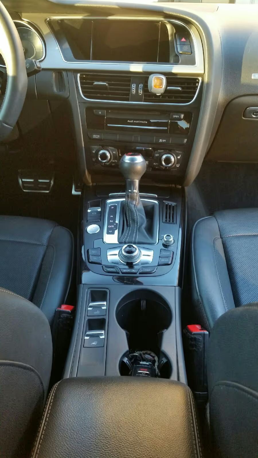 Car interior centered on a silver gear shift, dashboard, cup holders, and black seats.