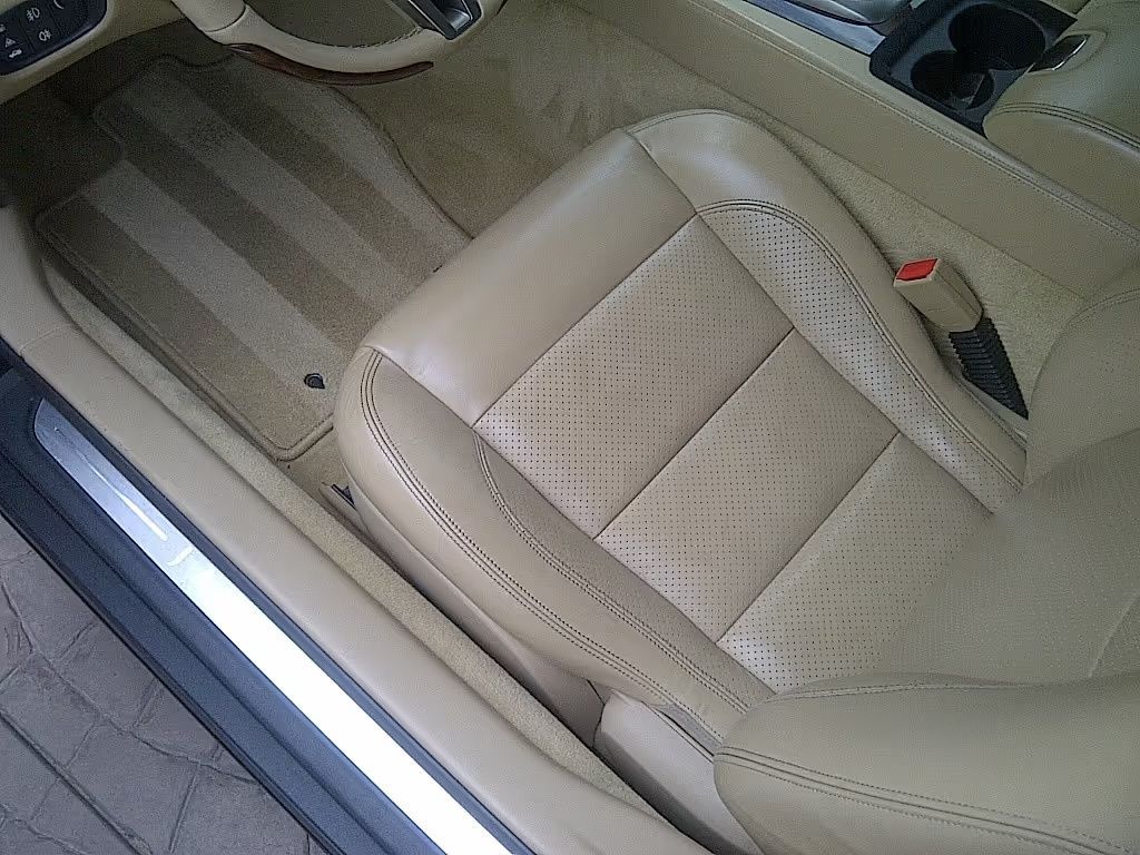 Beige car seat with patterned upholstery and red seatbelt latch in a vehicle interior