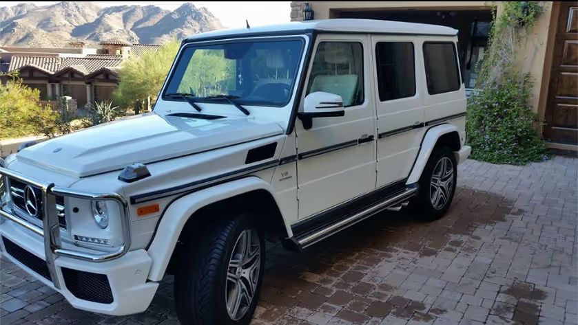 White Mercedes G-Class SUV parked on a brick driveway with mountains in the background