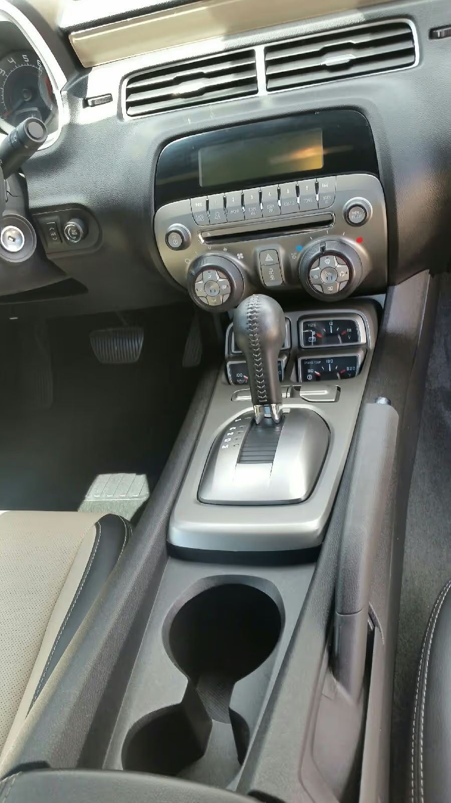 Car interior center console with radio, climate controls, gear shift, and cup holders
