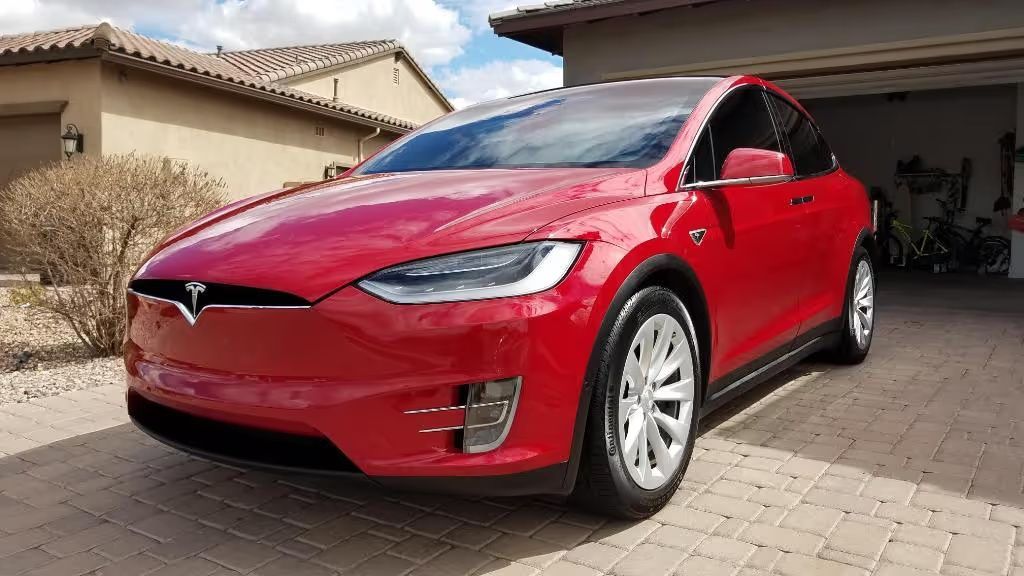Red Tesla SUV parked in a suburban driveway beside a house