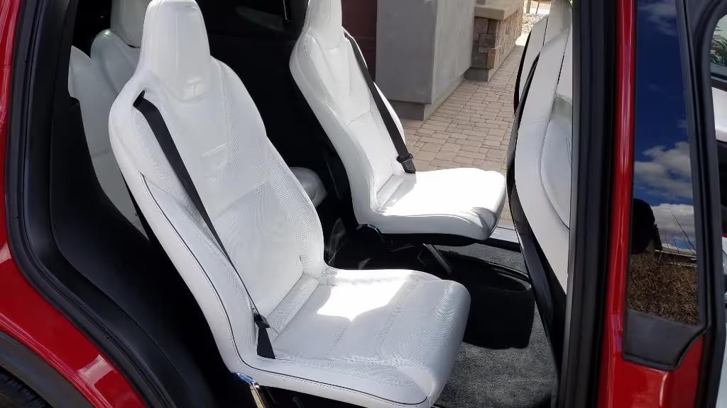 White car seats with black trim inside a red vehicle, viewed through an open door.