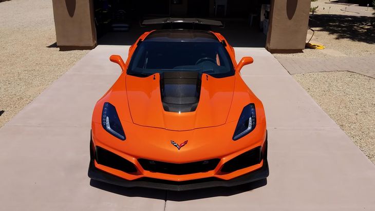 Orange sports car parked on a driveway, front view, with black hood and accents