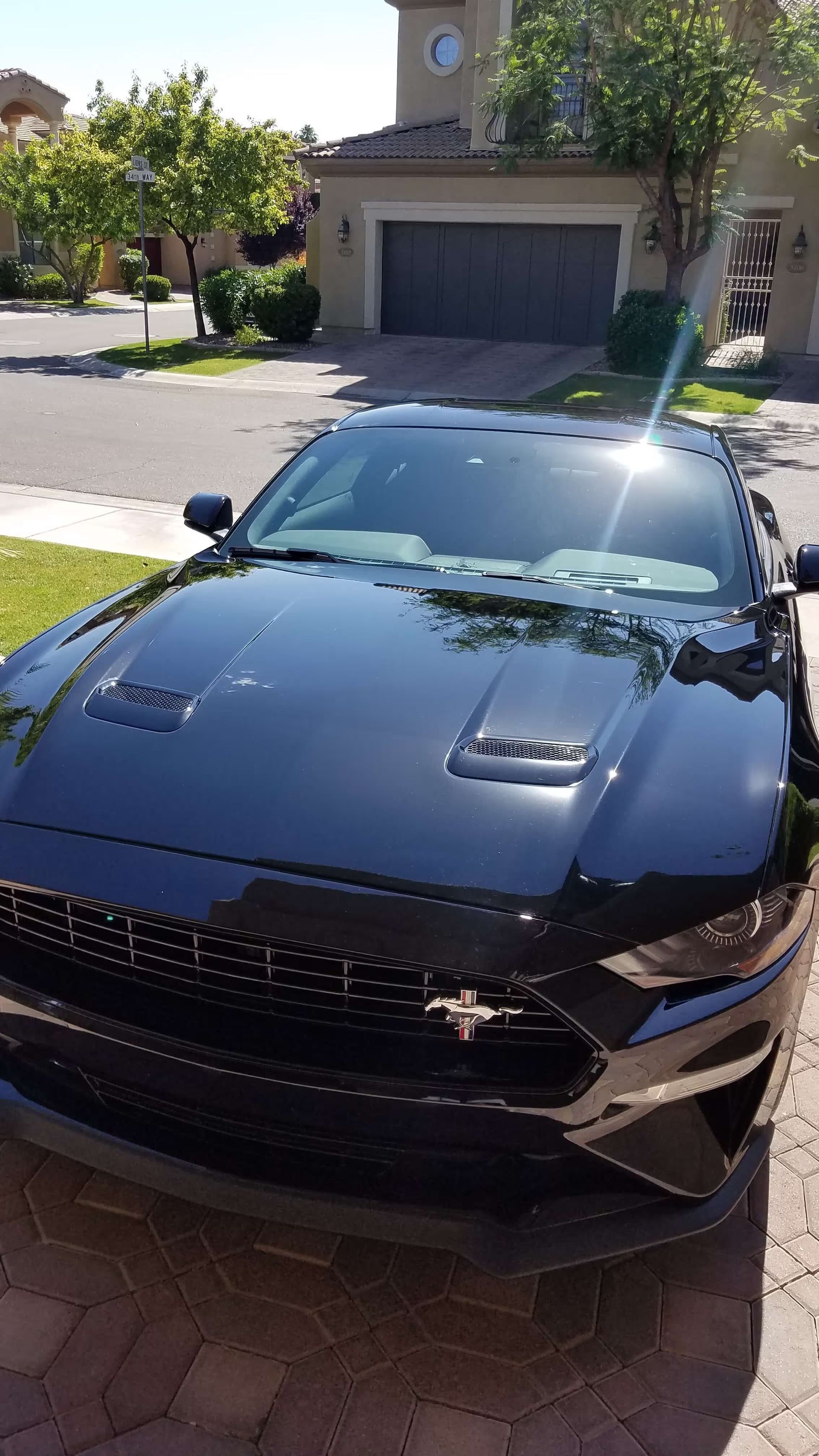 Black sports car parked in a sunny residential driveway, front view with garage and house in background