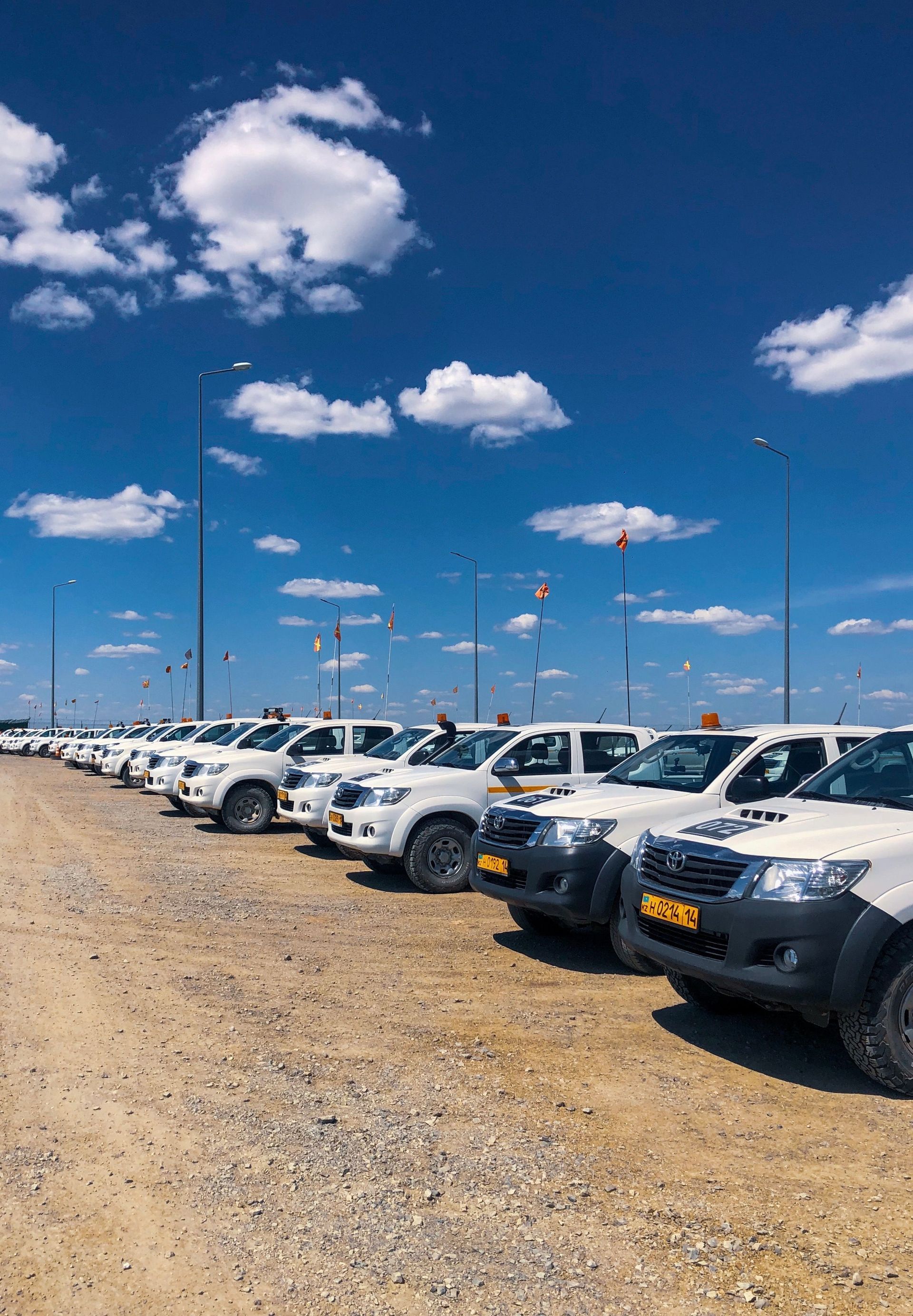 Rows of white pickup trucks parked on a gravel lot under a bright blue sky with clouds