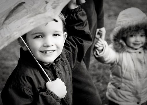A young boy holding an umbrella in one hand and the hand of a parent in the other. His sister takes the parent's other hand.