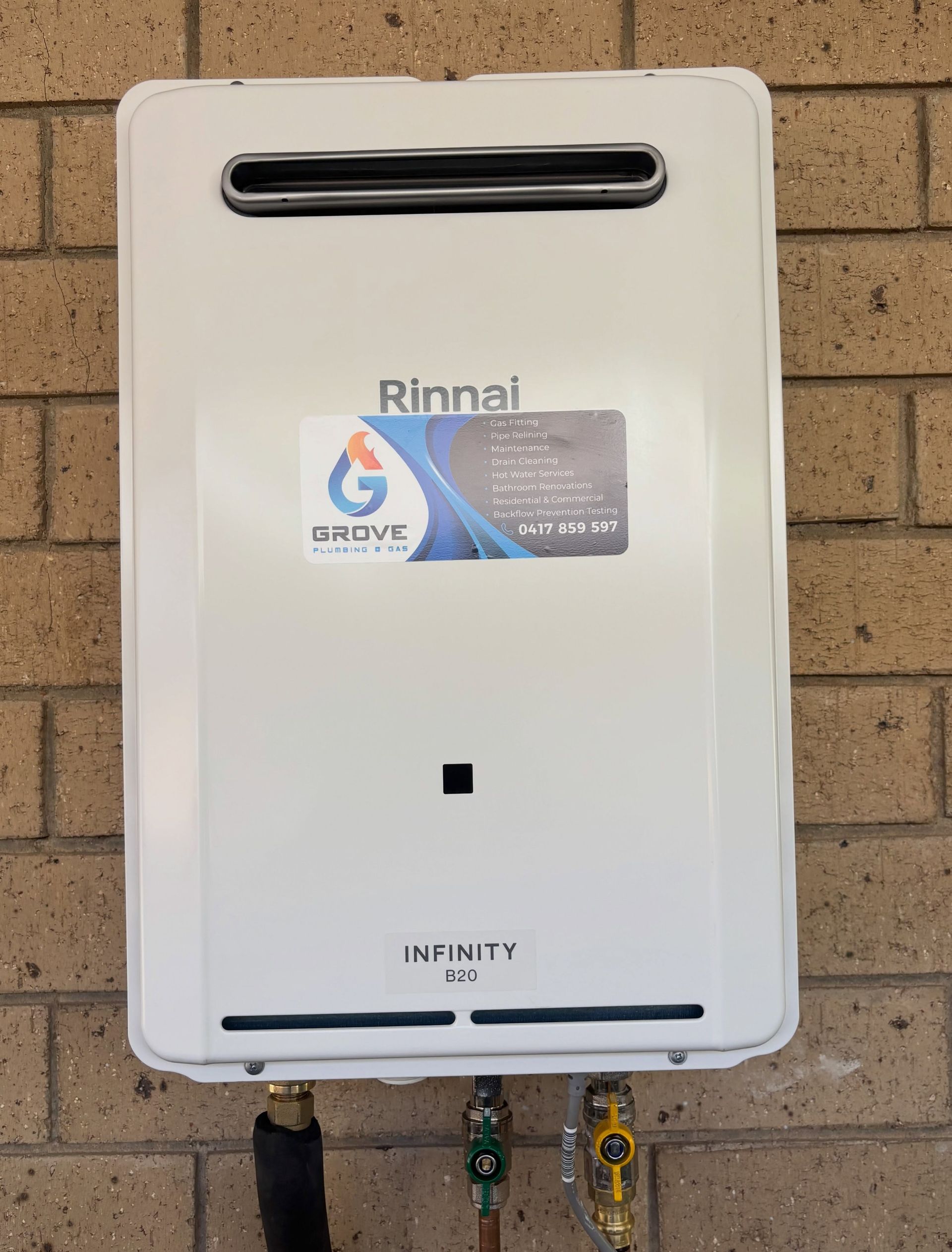 White Rinnai Infinity gas water heater mounted on a brick wall with pipes below