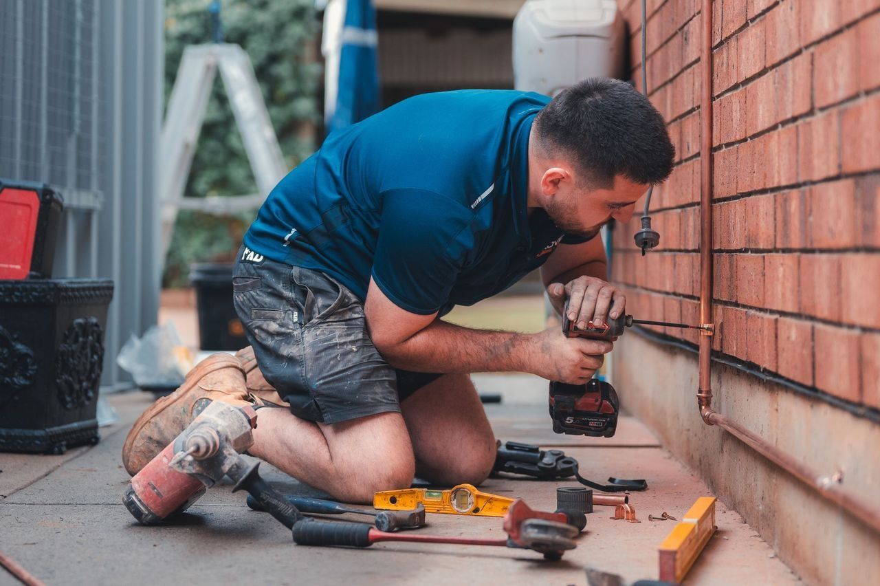 Worker kneeling beside a brick wall, using tools to install wiring outdoors.
