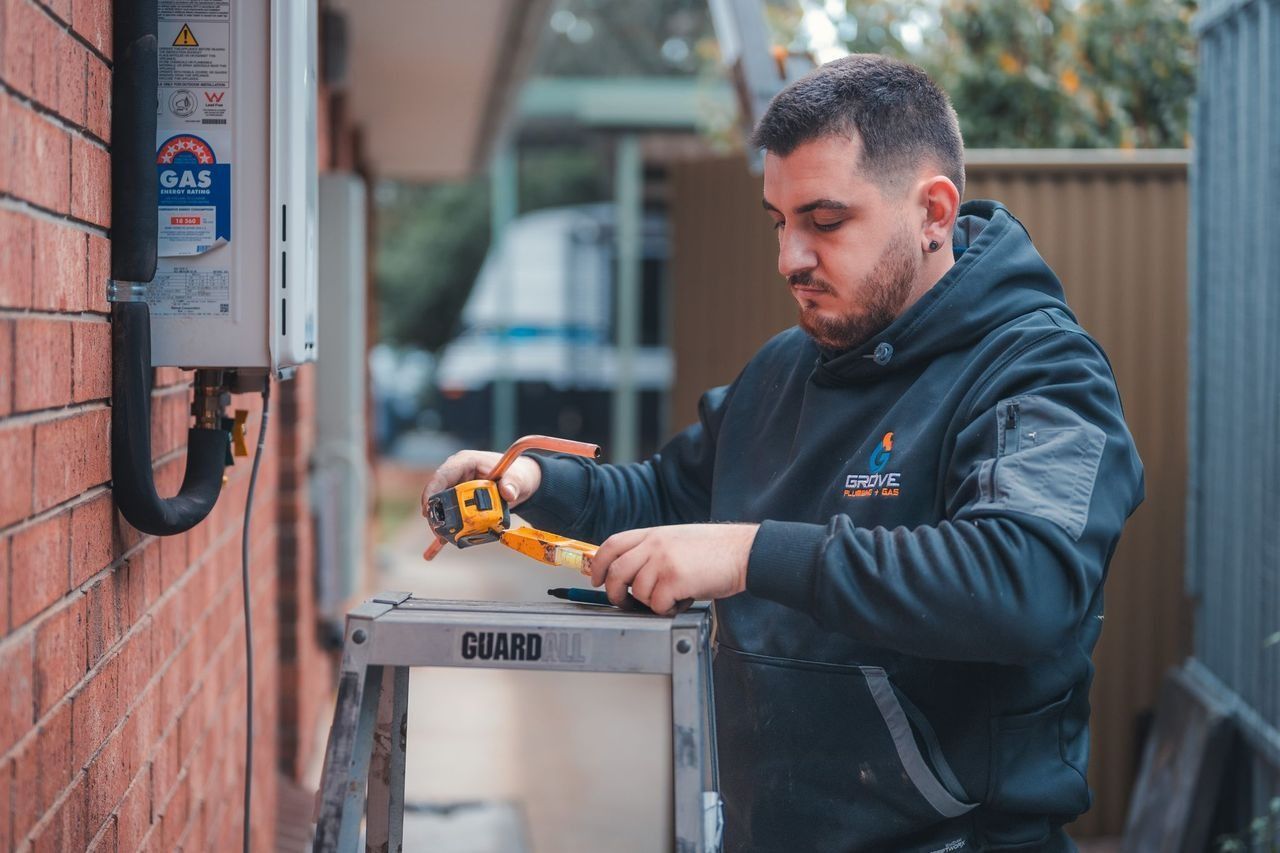 Technician using a power tool on an outdoor utility box beside a brick wall