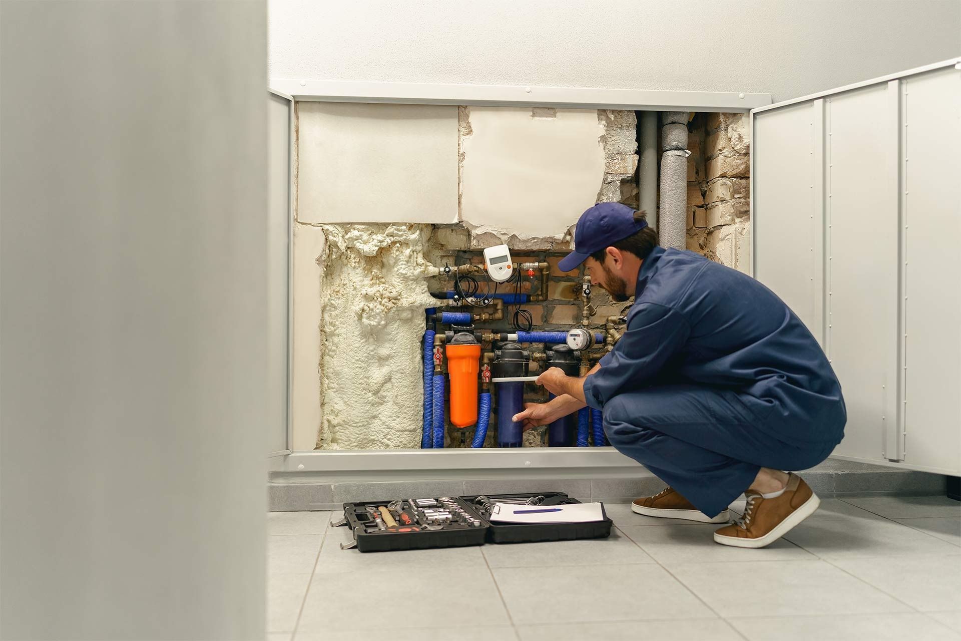 Person kneeling under a kitchen sink with a red toolbox on the floor, doing plumbing work.