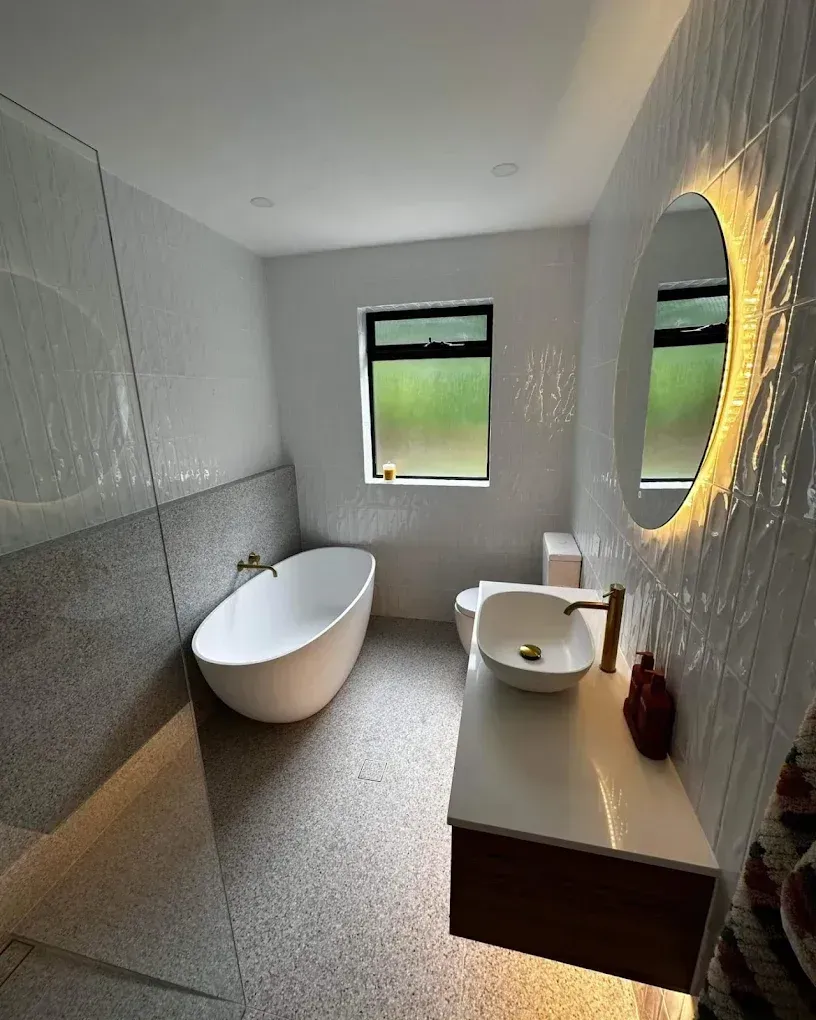 Modern bathroom with freestanding tub, wall mirror, sink vanity, and two windows overlooking green views
