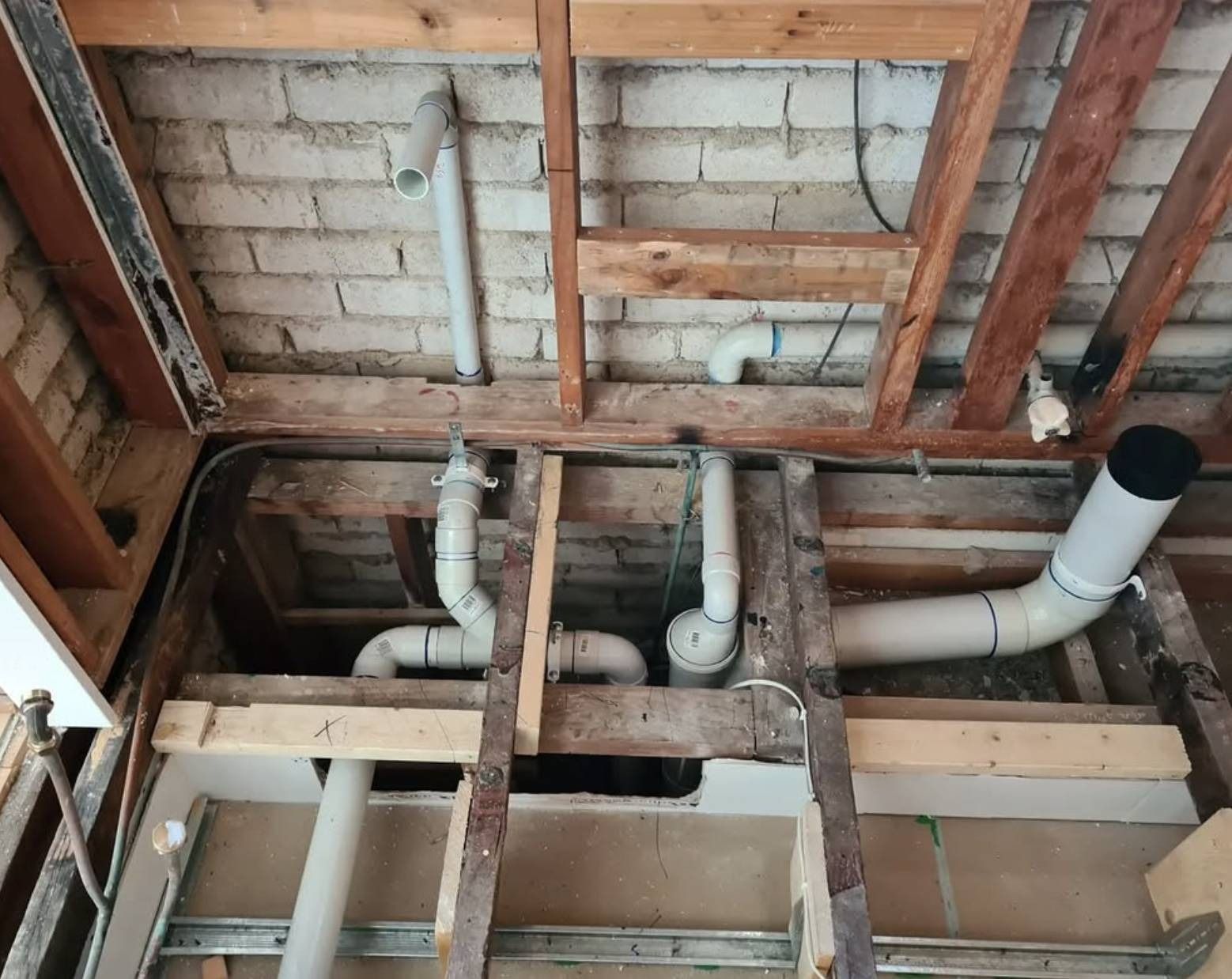 Exposed ceiling framing with white PVC plumbing pipes and unfinished brick and wood structure