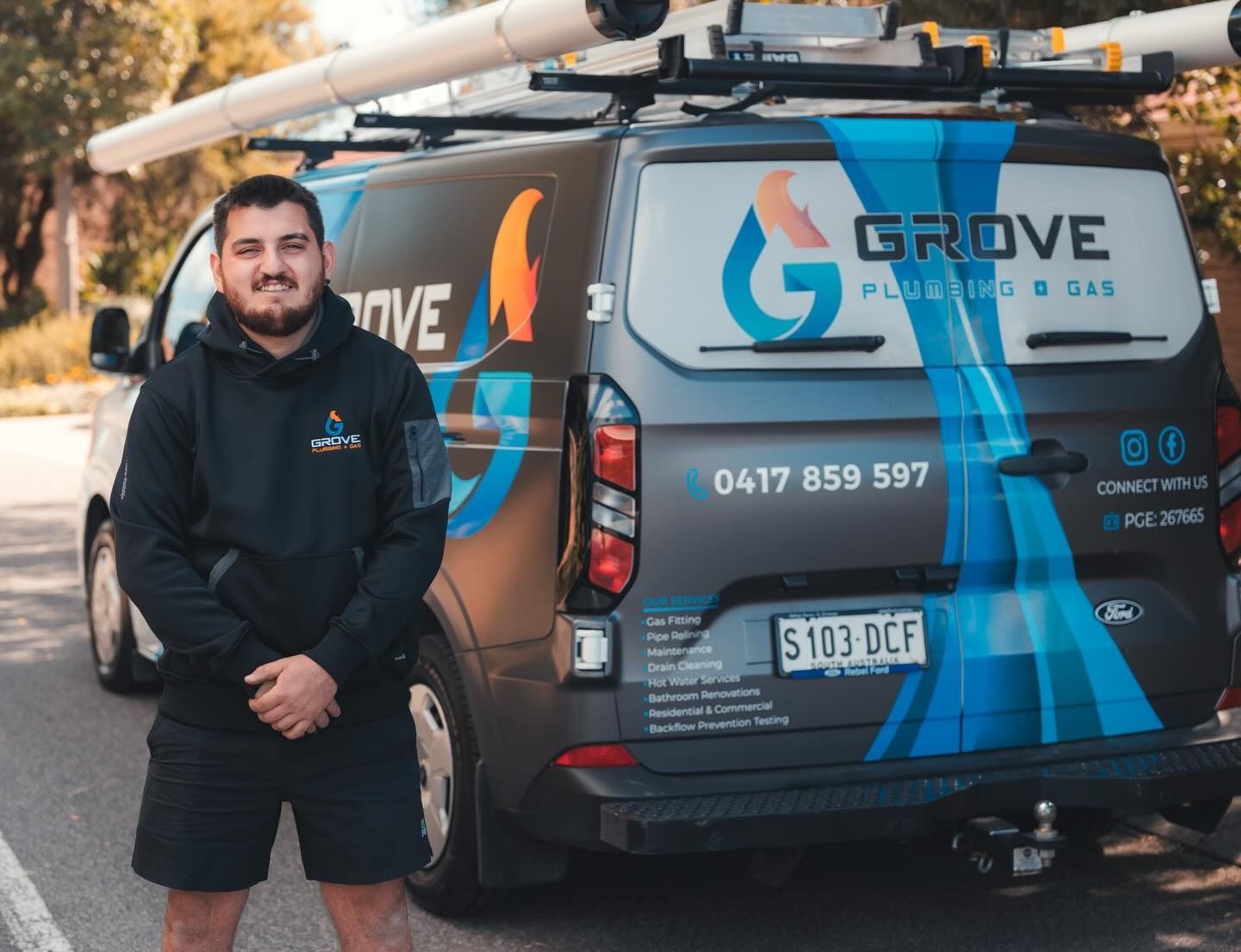 Man standing beside a blue-and-black GROVE Gas service van with roof pipes and company branding.