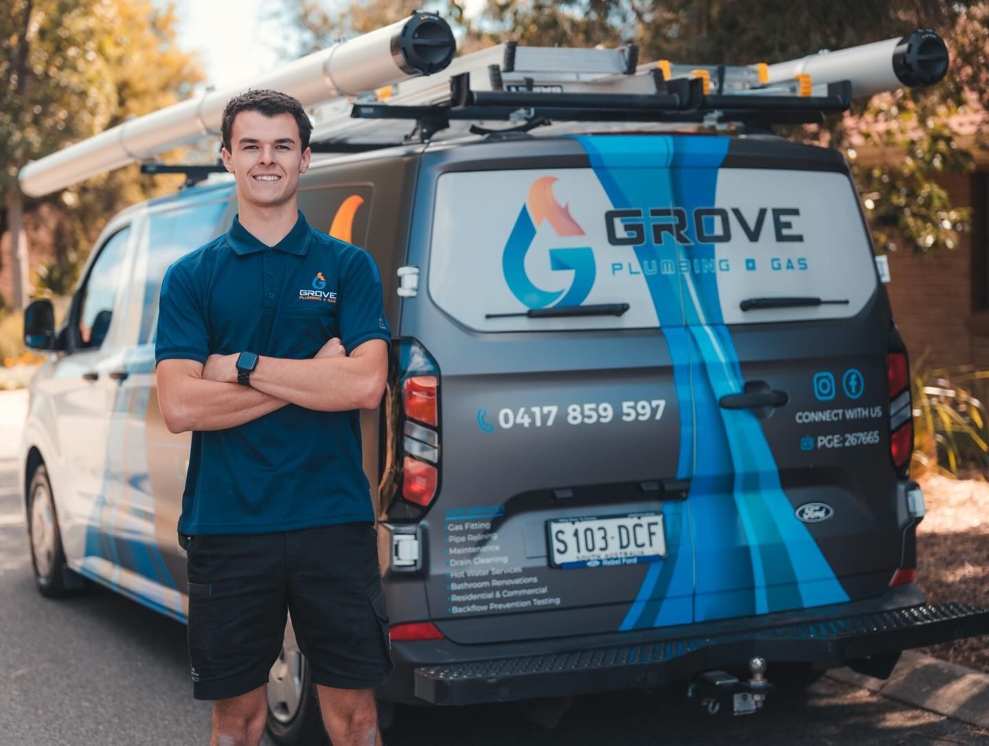 Tradesman standing beside a branded service van with ladders on top, smiling outdoors.