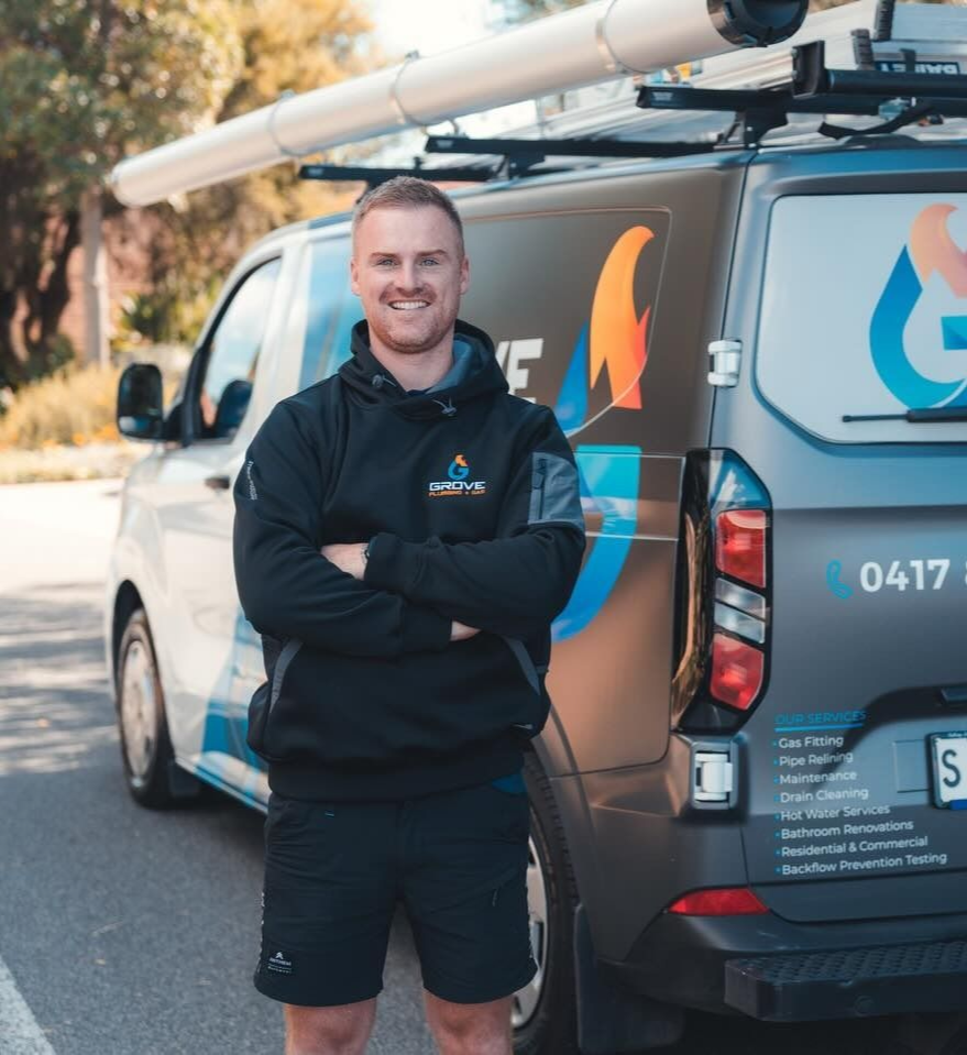 Smiling technician in black workwear standing by a branded service van with roof equipment.