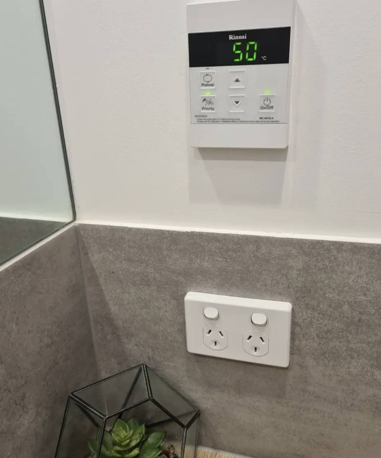 Wall-mounted thermostat and electrical outlet above gray tiled backsplash in a kitchen corner