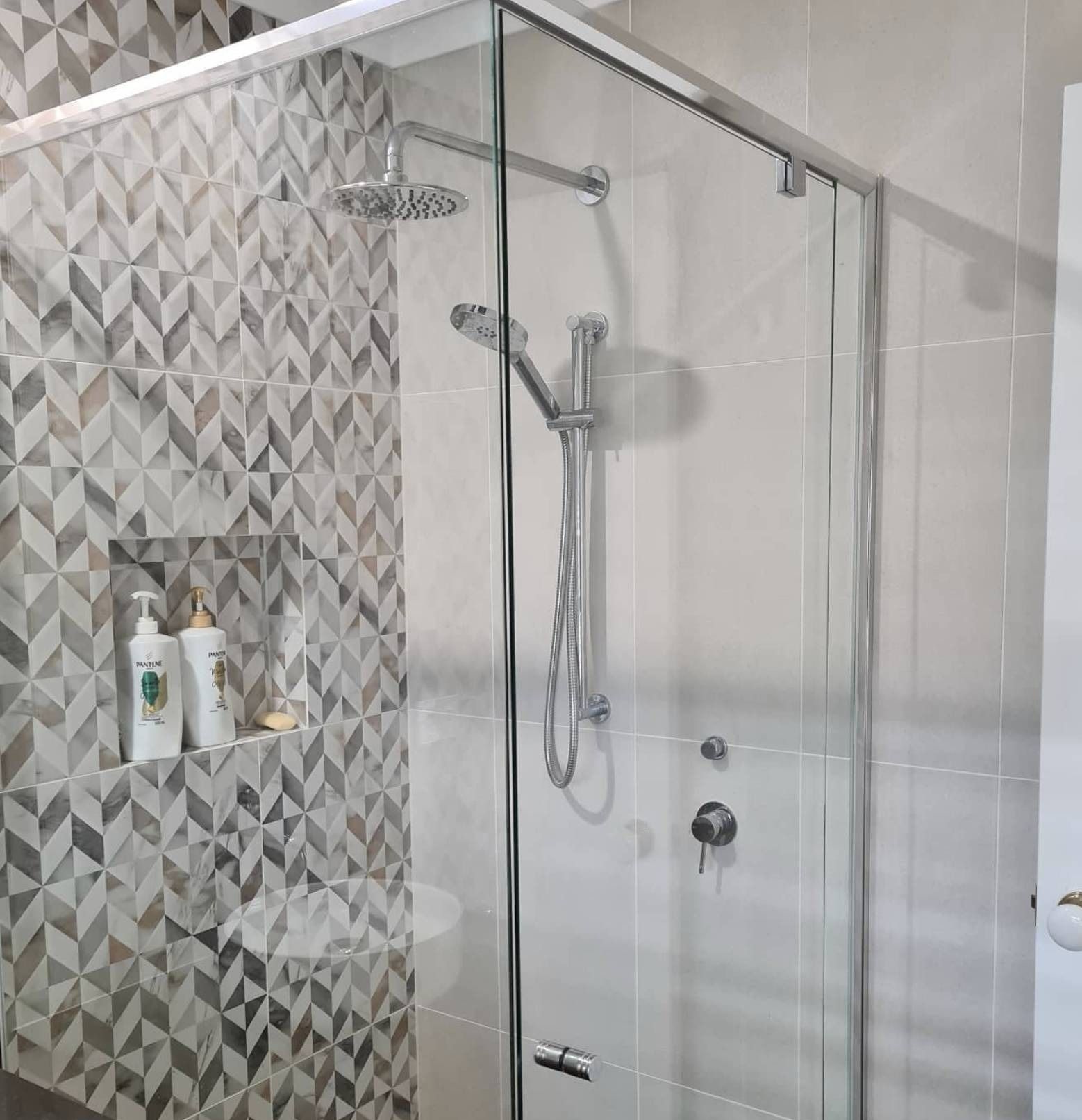 Modern shower with glass door, chrome fixtures, and gray geometric tile wall