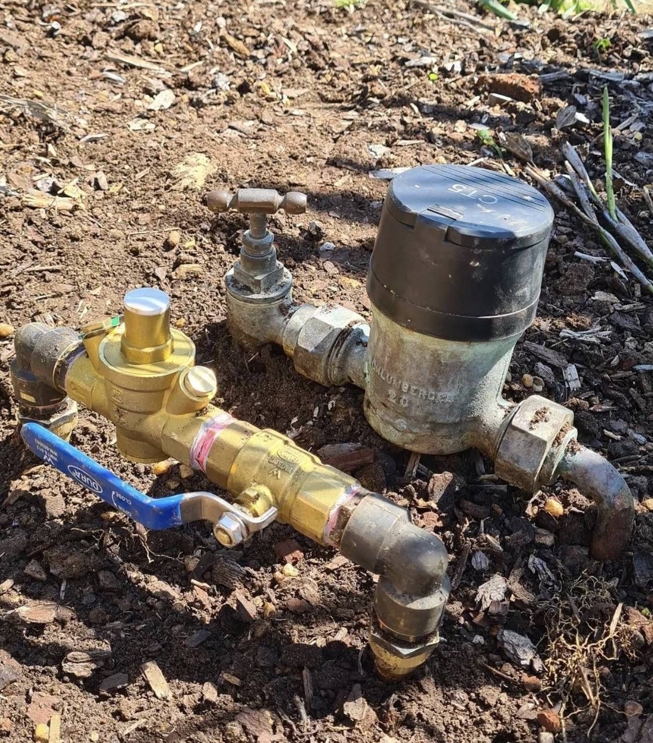 Brass irrigation valve assembly with blue lever and black cap on dirt ground outdoors