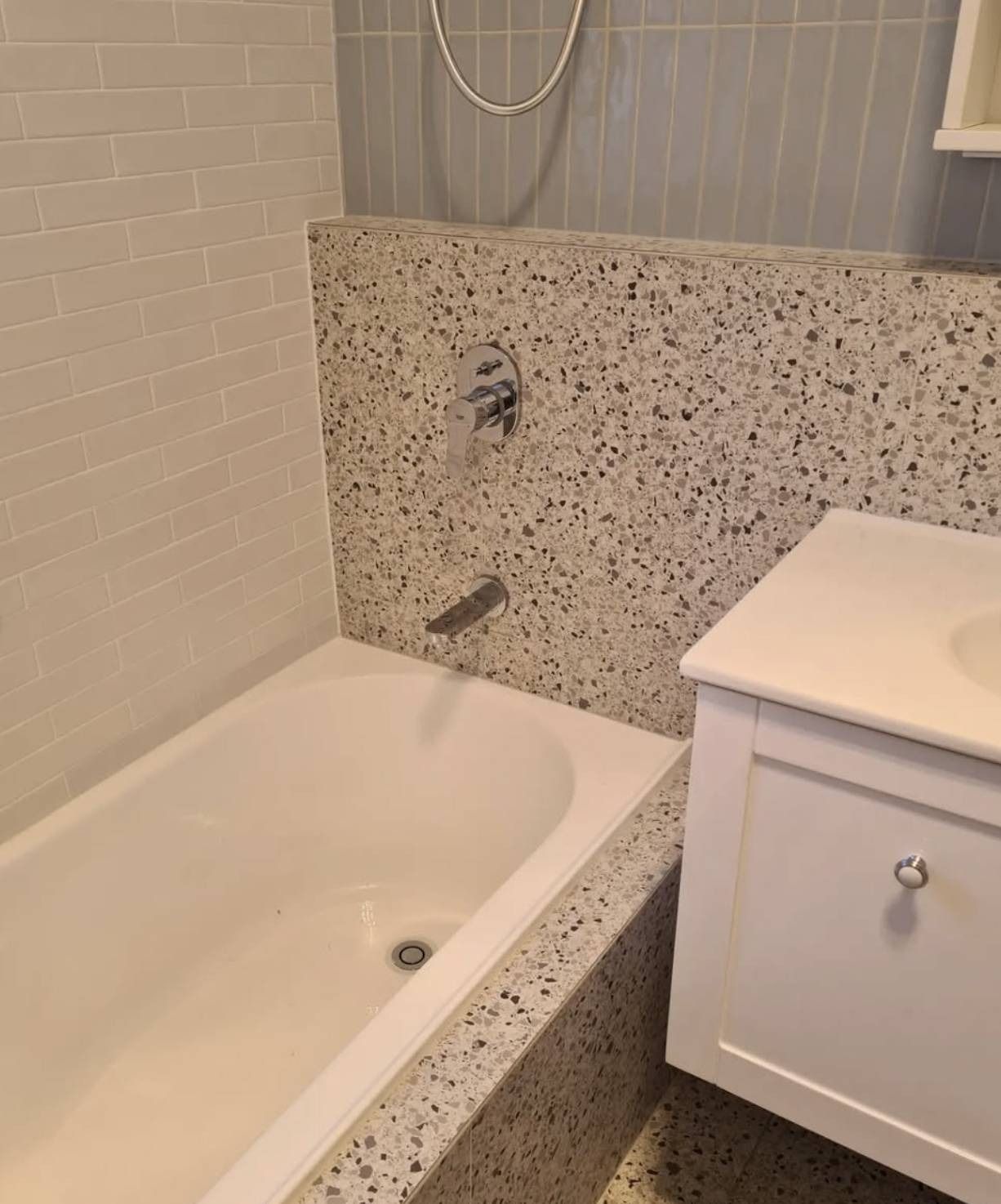 Compact bathroom with a speckled tub surround, white vanity, and tiled walls.