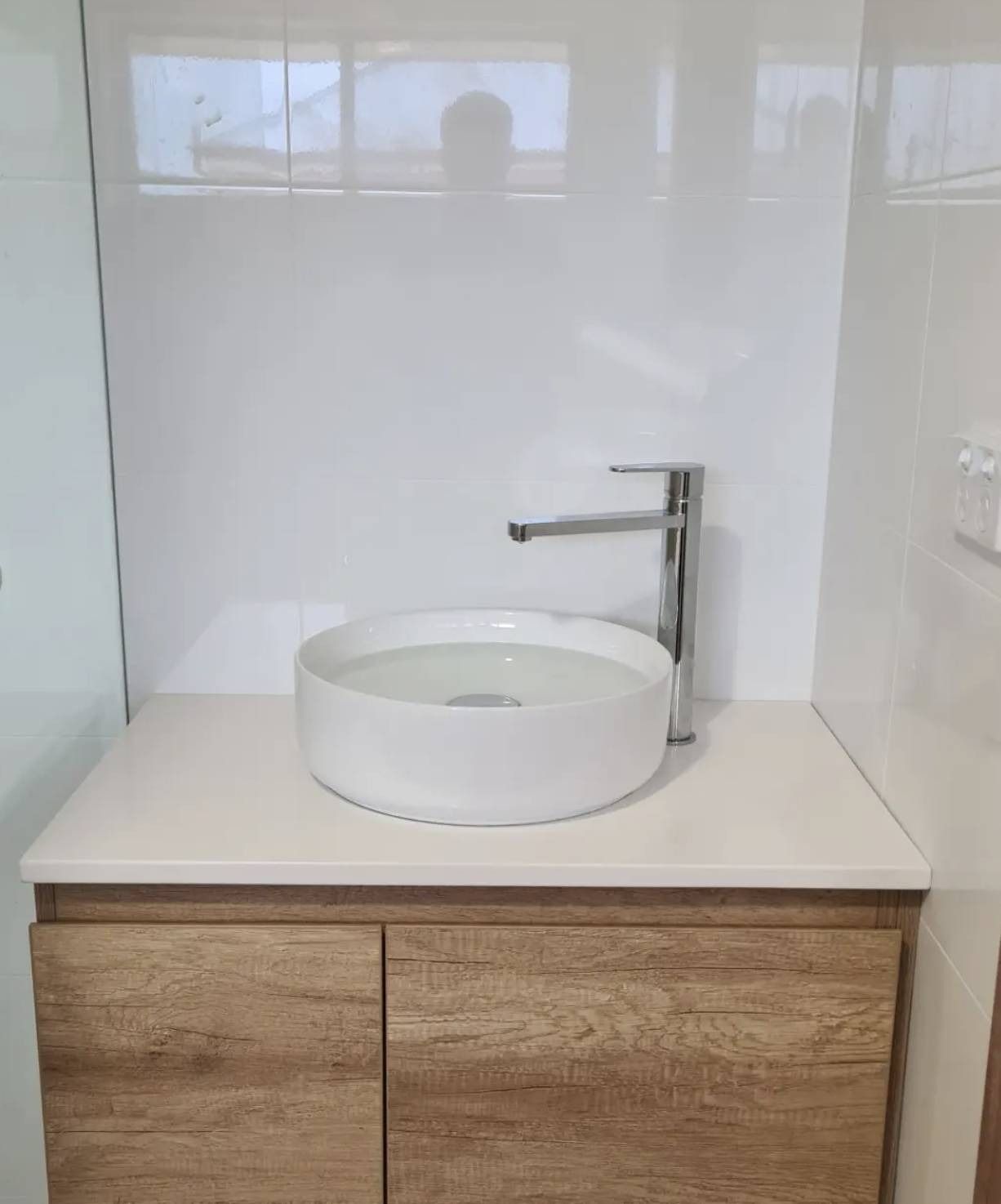 Modern bathroom vanity with round white vessel sink and chrome faucet on a wood cabinet.