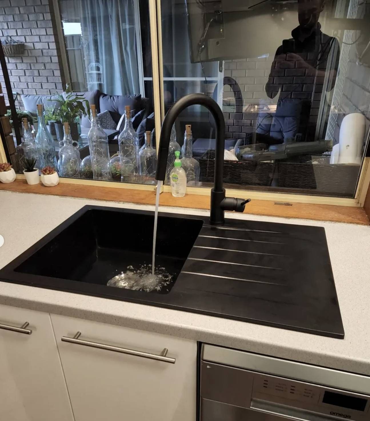 Modern kitchen sink with black faucet, black countertop, and window reflection above the counter