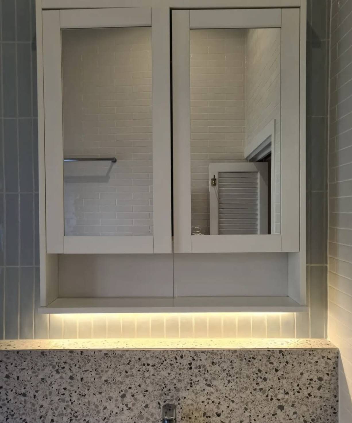 White kitchen wall cabinet with open glass doors and under-cabinet lighting above speckled countertop
